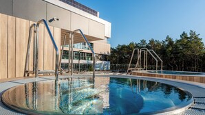 A modern outdoor swimming pool with metal ladders, surrounded by a wooden deck and a building with large windows. - Shellter Hotel Resort & Spa (Trzebiatow)