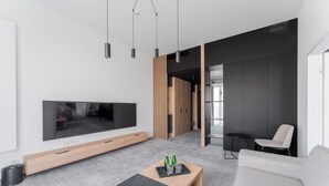 A modern living room with a flat-screen TV, a wooden coffee table with bottles, a grey sofa, and a black side table. - Shellter Hotel Resort & Spa (Trzebiatow)