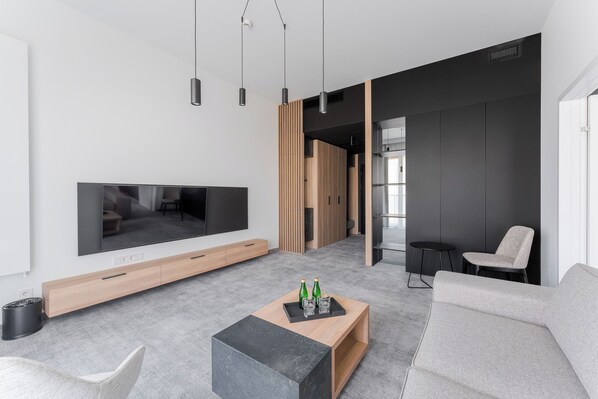 A modern living room with a flat-screen TV, a wooden coffee table with bottles, a grey sofa, and a black side table. - Shellter Hotel Resort & Spa (Trzebiatow)
