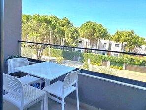 A balcony with a white table and chairs, a view of a residential area with trees and buildings.