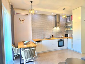 Una cocina moderna con un salpicadero de ladrillo, armarios blancos y un comedor con mesa de madera y sillas acolchadas.