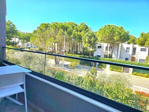 A balcony with a white chair, a railing, and a view of modern buildings and trees.