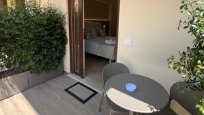 A sunlit outdoor area with a round table and chairs, a small potted plant, and a wooden door leading to a bedroom. - Residenza Gurnea - Free Private Parking (Tropea)