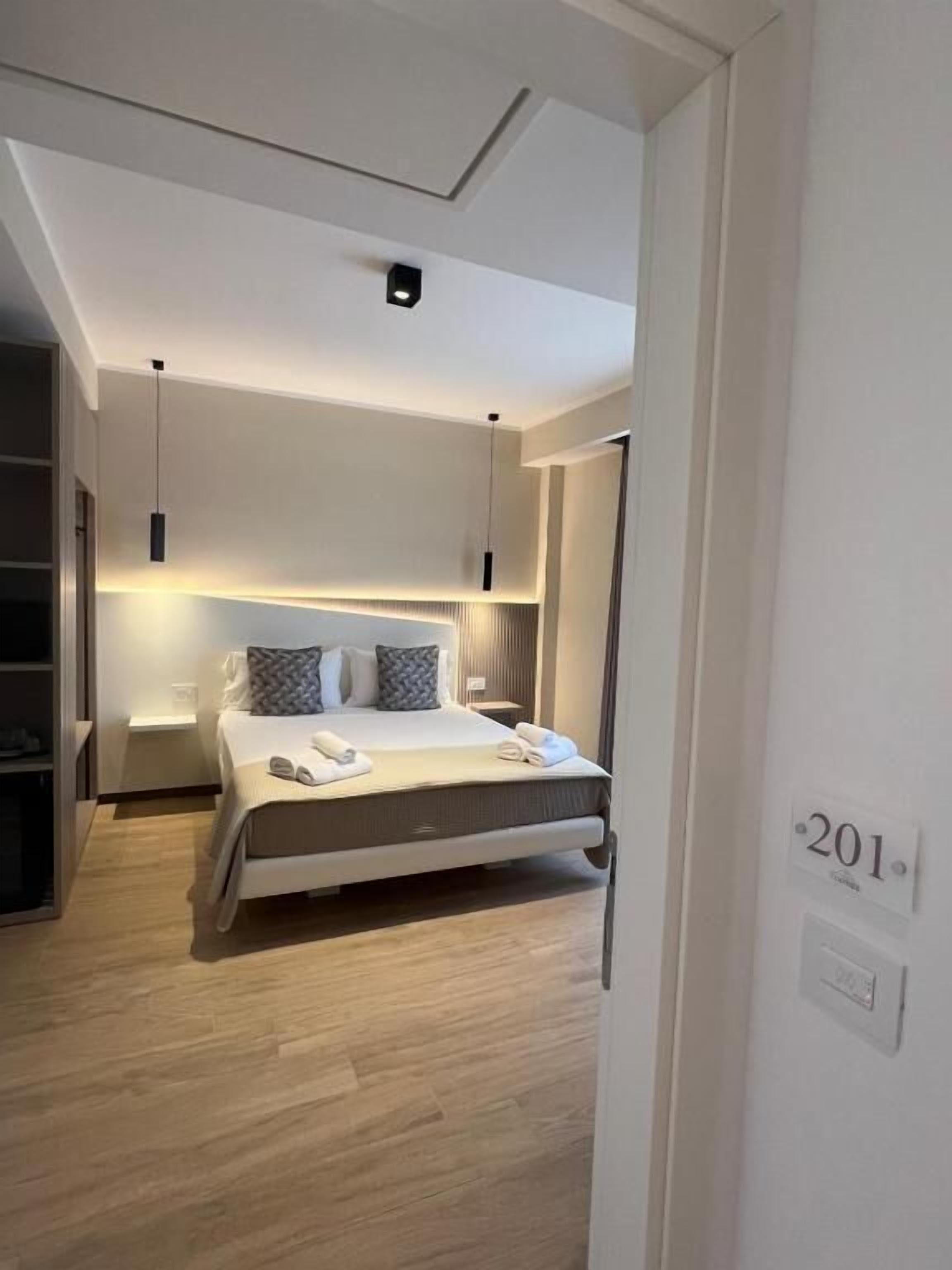 A modern hotel room with a bed, bedside tables, and a ceiling light fixture.