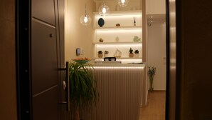 A reception desk with a modern design, featuring a light wood finish and a glass top. There are multiple shelves above the desk displaying decorative items and plants. - Residenza Gurnea - Free Private Parking (Tropea)