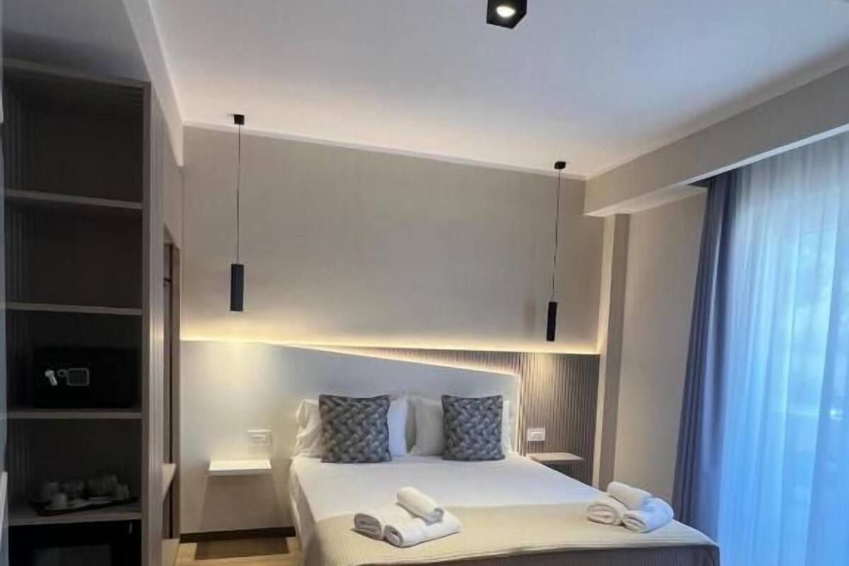 Een moderne hotelkamer met een groot bed, inbouwplanken en een groot raam met gordijnen.