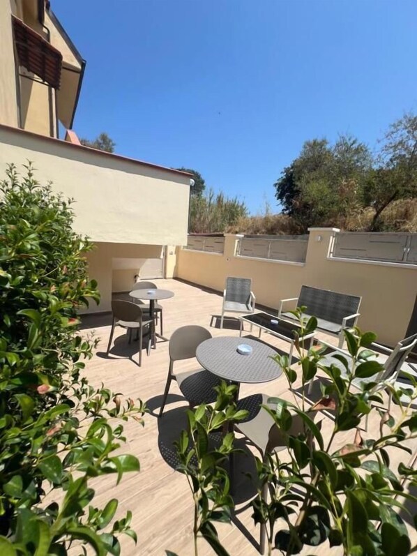 An outdoor patio with tables and chairs, surrounded by greenery and a building. - Residenza Gurnea - Free Private Parking (Tropea)