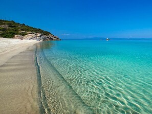 A beach with clear turquoise water, a sandy shore, and rocky terrain.