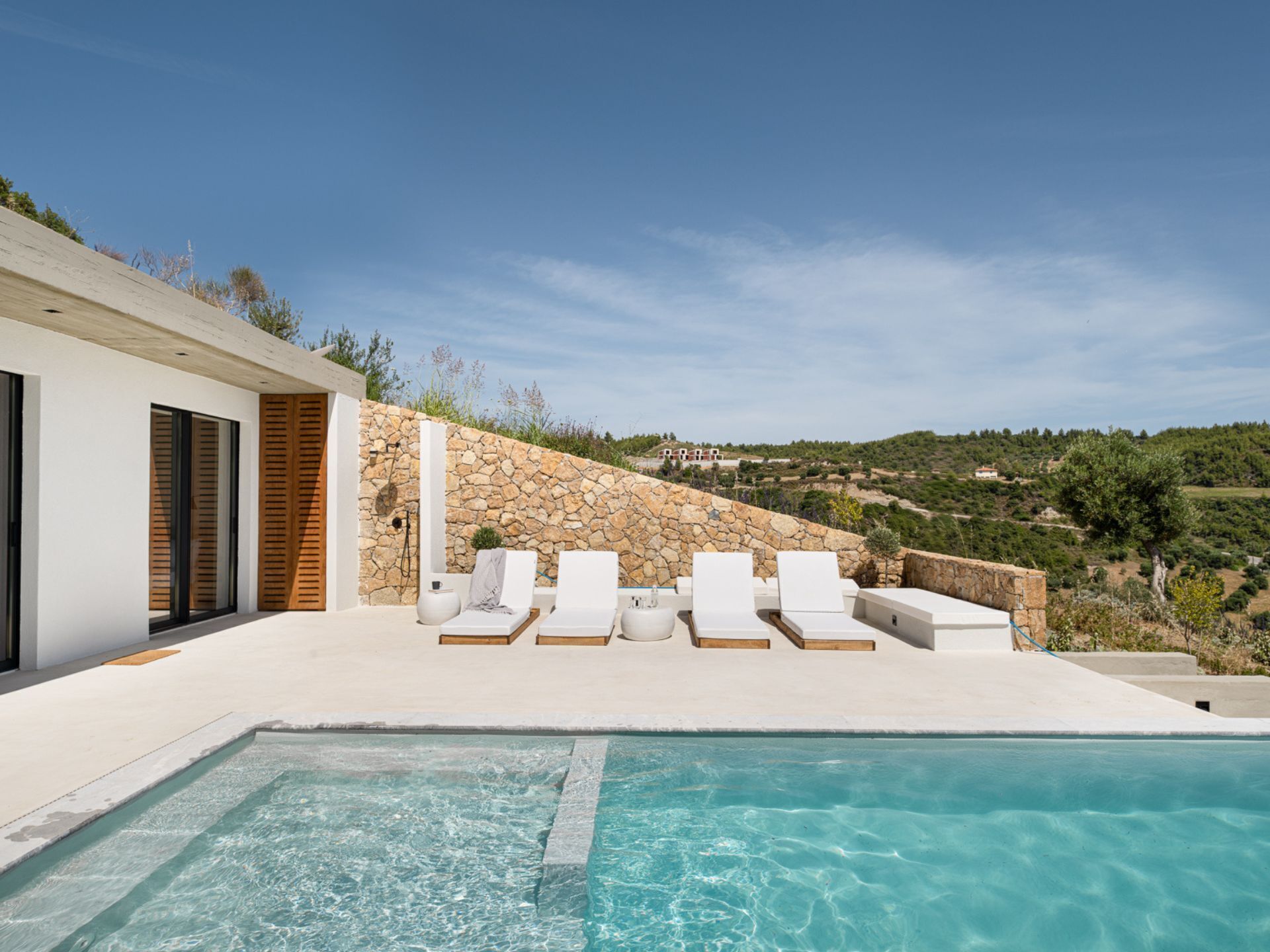Un espace piscine extérieur moderne, doté de chaises longues et d’un mur en pierre en arrière-plan.