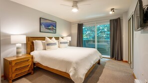 A bedroom with a bed, nightstands, a ceiling fan, a painting, and a window with curtains.