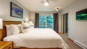 A hotel room with a large bed, a headboard, a painting, a ceiling fan, and a television.