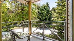 A covered outdoor area with a railing, a bench, and a view of a forested area.