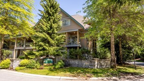 A two-story house with a balcony, surrounded by trees and a stone wall.