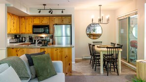 A modern kitchen with wooden cabinets, stainless steel appliances, and a dining area with a round table and chairs.