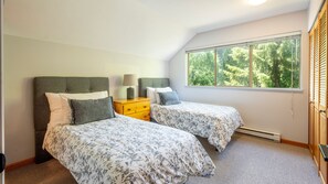 Une chambre avec deux lits, une table de chevet, une fenêtre donnant sur des arbres et un radiateur.