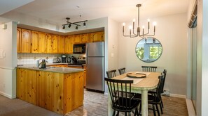 A modern kitchen with wooden cabinets, stainless steel appliances, and a dining area with a wooden table and chairs.