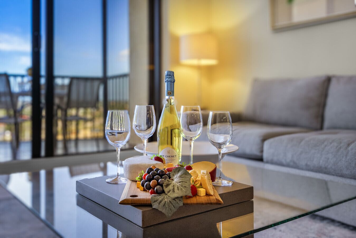 Una mesa con botella de vino, copas, tabla de quesos, uvas y fresas.