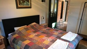 A neatly made bed with a colorful quilt, a small bedside table, and a door leading to a hallway. - Holiday Home Saniv (Batina)