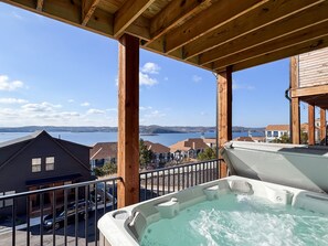 Ein Whirlpool auf einer Holzterrasse mit Blick auf einen See und Häuser im Hintergrund.