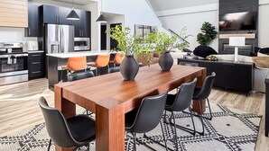 A modern kitchen with stainless steel appliances, a dining area with a wooden table and black chairs, and a living area with a sofa and a TV. - Copper Pointe | Lake view, Hot tub, Theatre, Pool table, Dog-friendly (Hollister)