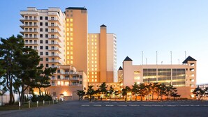 Un hotel moderno con varios pisos, un estacionamiento y un edificio de cristal grande al fondo.