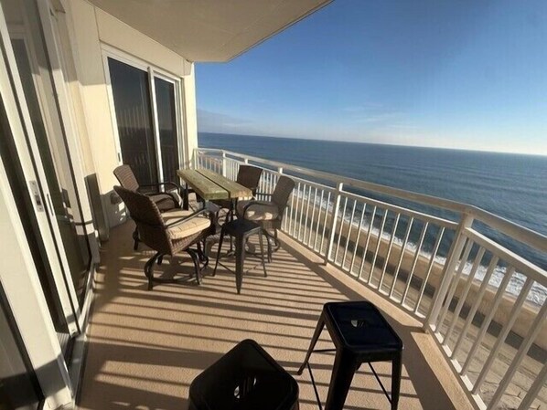 A balcony with a view of the ocean, furnished with chairs and a table.