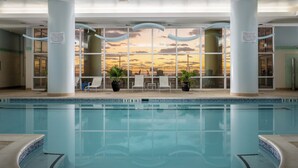 Una piscina interior con vistas al atardecer, sillas de descanso y plantas en macetas.