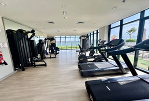 A gym with cardio machines, weight training equipment, and large windows offering a view of the outdoors.