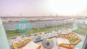 A balcony with wicker chairs and a small table, overlooking a construction site and a highway. - Bloomfields Fantastic STU Azizi Riviera (Dubai)