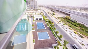 A high-rise building with a rooftop pool area, a landscaped garden, and a view of a highway and power lines. - Bloomfields Fantastic STU Azizi Riviera (Dubai)
