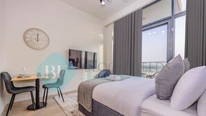 A modern hotel room with a bed, a desk with chairs, a TV, and a large window. - Bloomfields Fantastic STU Azizi Riviera (Dubai)