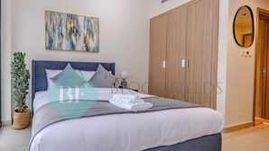 A neatly made bed with a grey headboard, a potted plant, and a wall-mounted abstract painting. - Bloomfields Fantastic STU Azizi Riviera (Dubai)