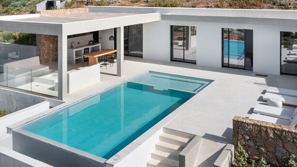 A modern house with a large swimming pool, outdoor seating, and a stone wall. - Design Villa Skioni by Halkidiki Villas (Kassandra)