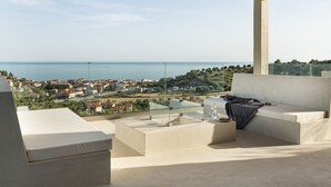 A modern outdoor seating area with a view of the sea and a town in the distance. - Design Villa Skioni by Halkidiki Villas (Kassandra)