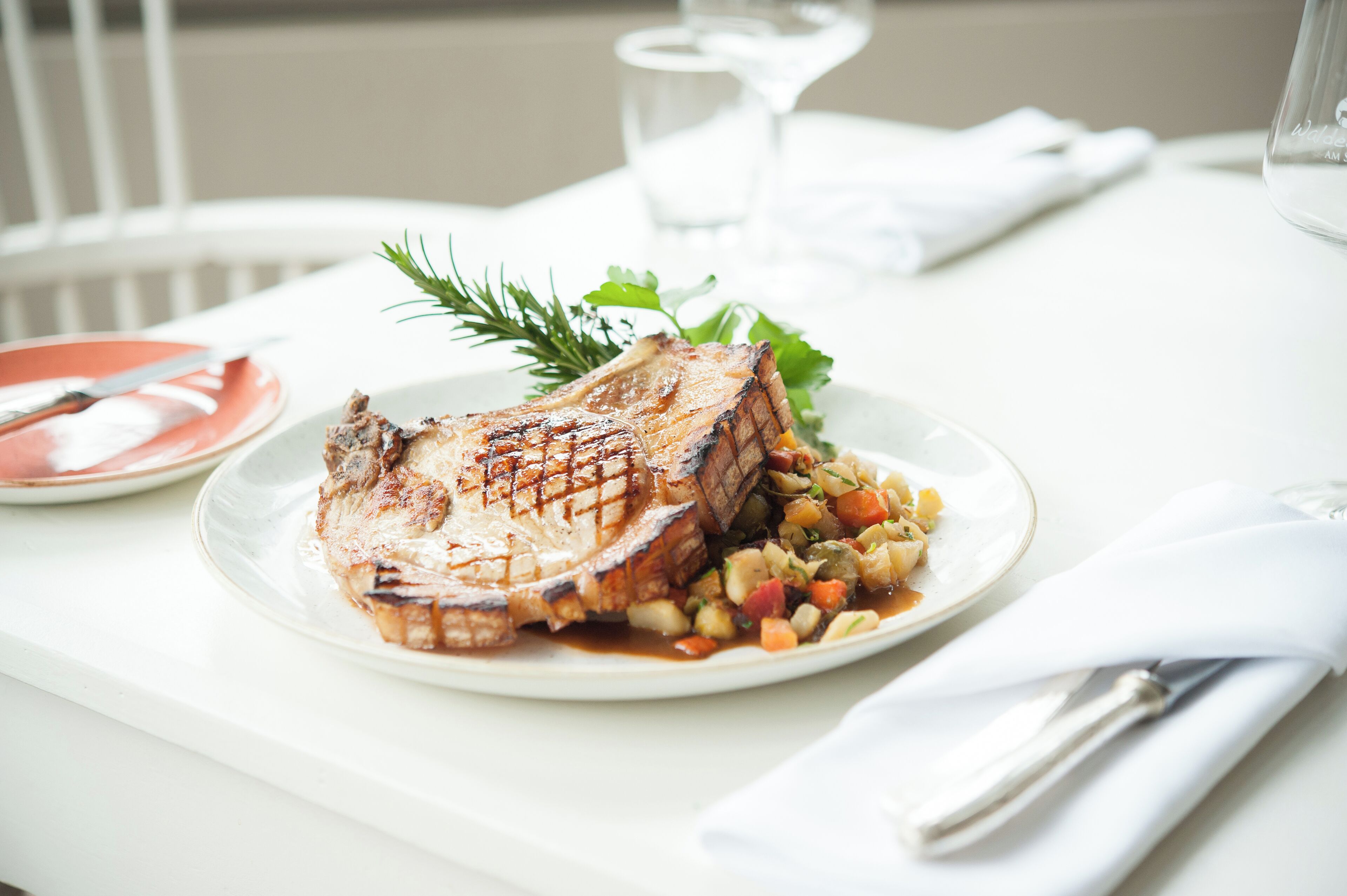 A plate of grilled meat with vegetables and a glass of water on a white table.