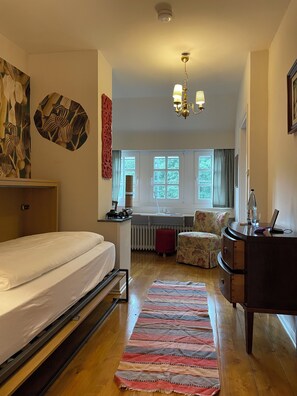 A bedroom with a bed, a desk, a chair, a dresser, and a window with curtains. - WaldesRuh am See (Aumuehle)