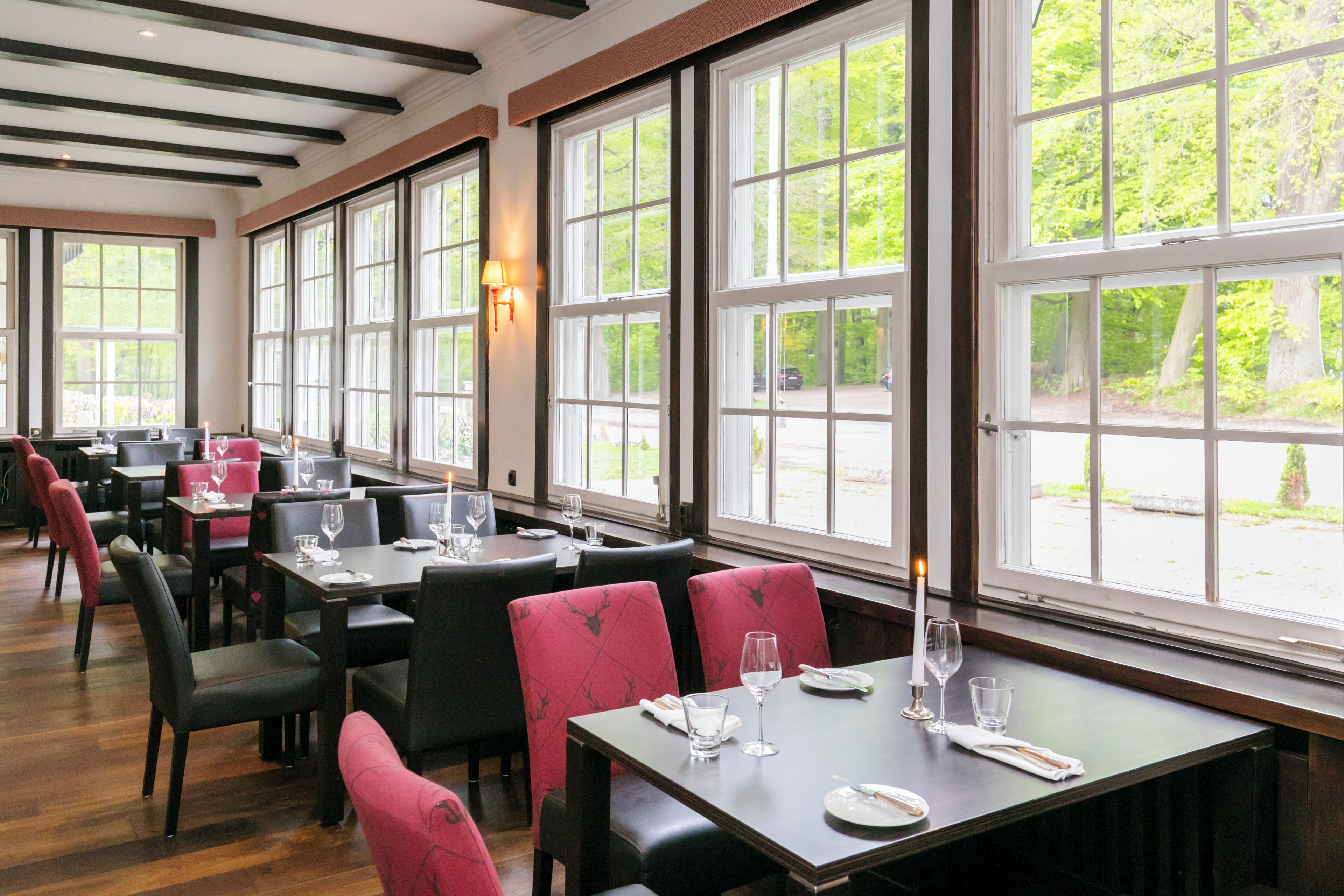 Ein Restaurant mit großen Fenstern, Holzböden und schwarzen und roten Polsterstühlen.