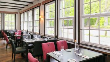 Ein Restaurant mit großen Fenstern, Holzböden und schwarzen und roten Polsterstühlen.
