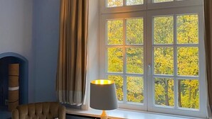 A room with a large window, a chair, and a table lamp.