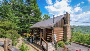 A log cabin with a stone chimney, wooden exterior, and a porch with steps leading to a deck. - Clean and cozy one bedroom for 2- mountain view, hot tub, cute as can be! (Gatlinburg)