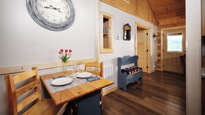 A wooden dining table with plates, glasses, and a vase of red flowers. A clock is on the wall, and a mirror hangs above a door. - Clean and cozy one bedroom for 2- mountain view, hot tub, cute as can be! (Gatlinburg)