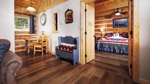 A cozy cabin interior with a dining area, a blue bench, a bed with a colorful quilt, and wooden walls and floors. - Clean and cozy one bedroom for 2- mountain view, hot tub, cute as can be! (Gatlinburg)
