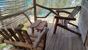 A wooden deck with a bench and a table, overlooking a beach with trees and the ocean. - Ecolodge Anjomba (Taolagnaro)