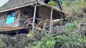 A rustic wooden house with a steeply pitched roof, a balcony, and a window with a blue frame. - Ecolodge Anjomba (Taolagnaro)