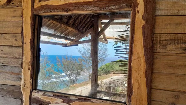 A rustic wooden cabin with a large window overlooking a coastal landscape. - Ecolodge Anjomba (Taolagnaro)