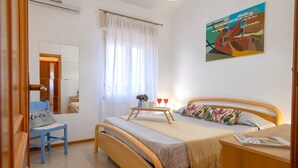 A bedroom with a bed, a chair, a bedside table, a mirror, and a painting on the wall. - Sardinia Re - Lido 68 (Alghero)