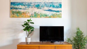 A wooden cabinet with a television on top, a painting above it, and two potted plants on either side. - Sardinia Re - Lido 68 (Alghero)