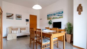 A dining area with a wooden table and chairs, a television, and a painting on the wall. - Sardinia Re - Lido 68 (Alghero)