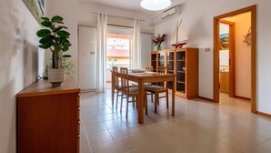 A dining area with a wooden table and chairs, a potted plant, and a cabinet with glass doors. - Sardinia Re - Lido 68 (Alghero)