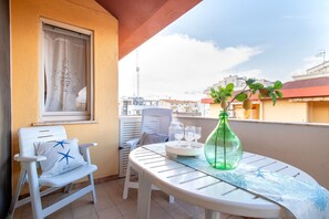 A balcony with a white chair, a table with a green bottle, and a window with a curtain. - Sardinia Re - Lido 68 (Alghero)